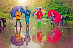 Little boys and girl happily walking under umbrella in park